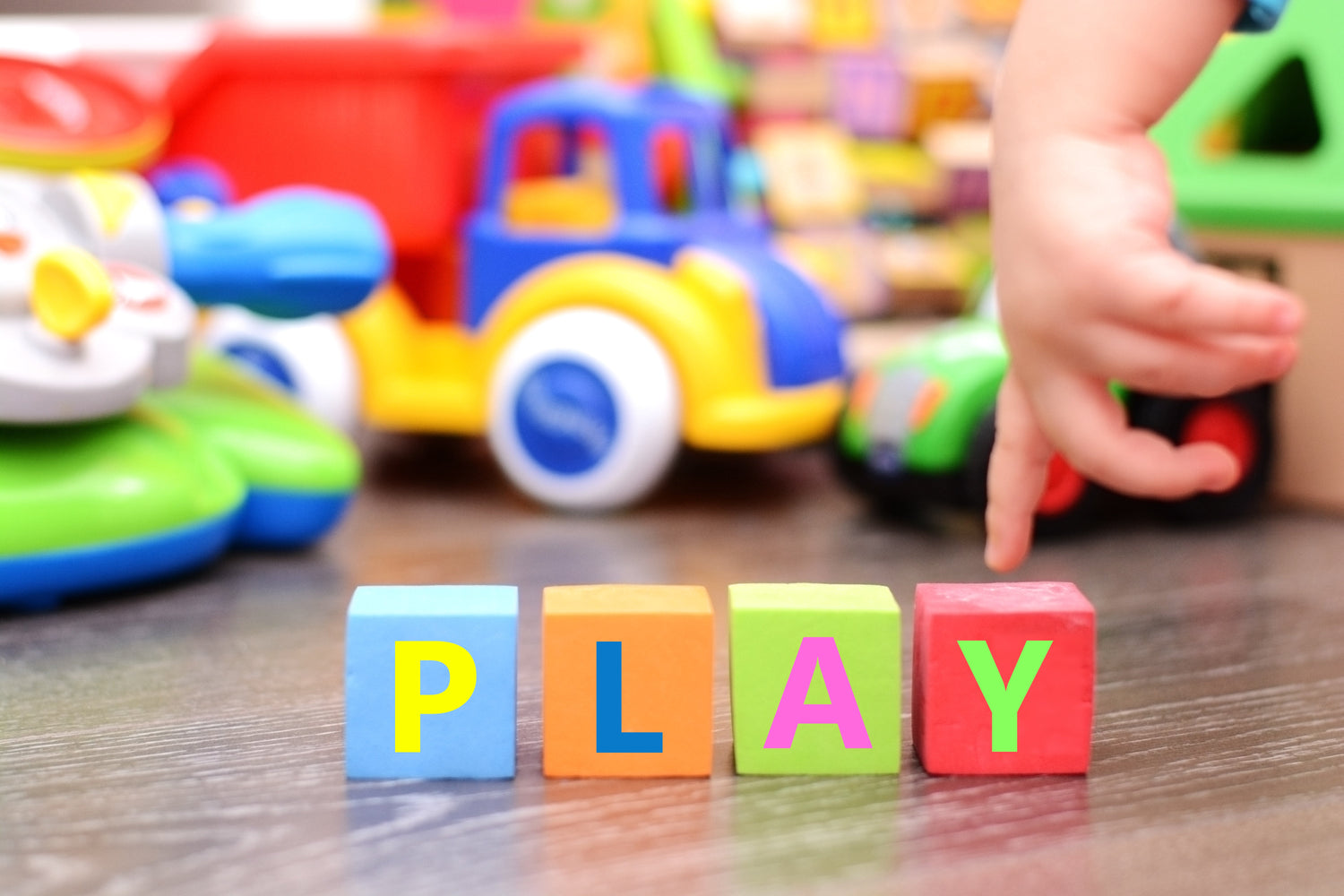 Blocs de lettres colorés formant le mot PLAY avec des jouets pour bébé en arrière-plan