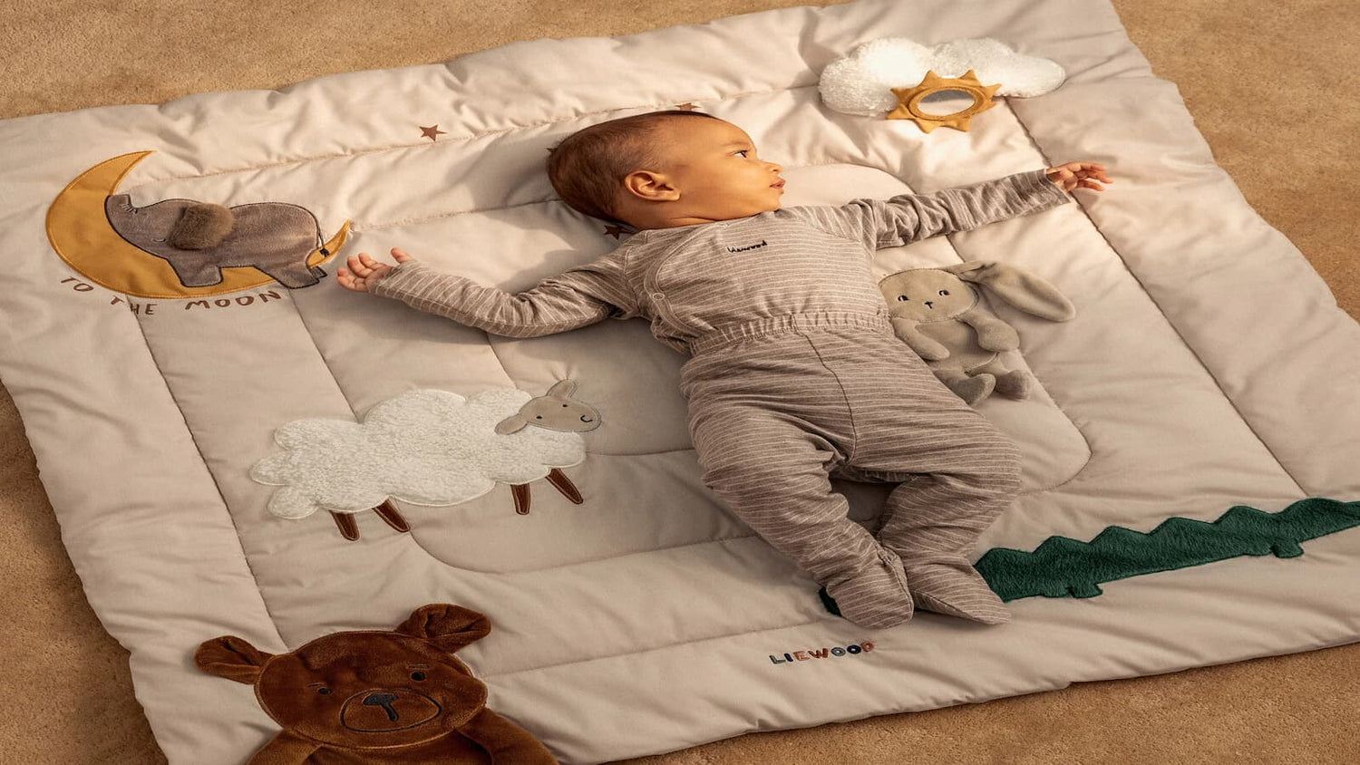 « Bébé allongé sur un tapis de sol Liewood, jouant tranquillement dans un espace d’éveil confortable. »