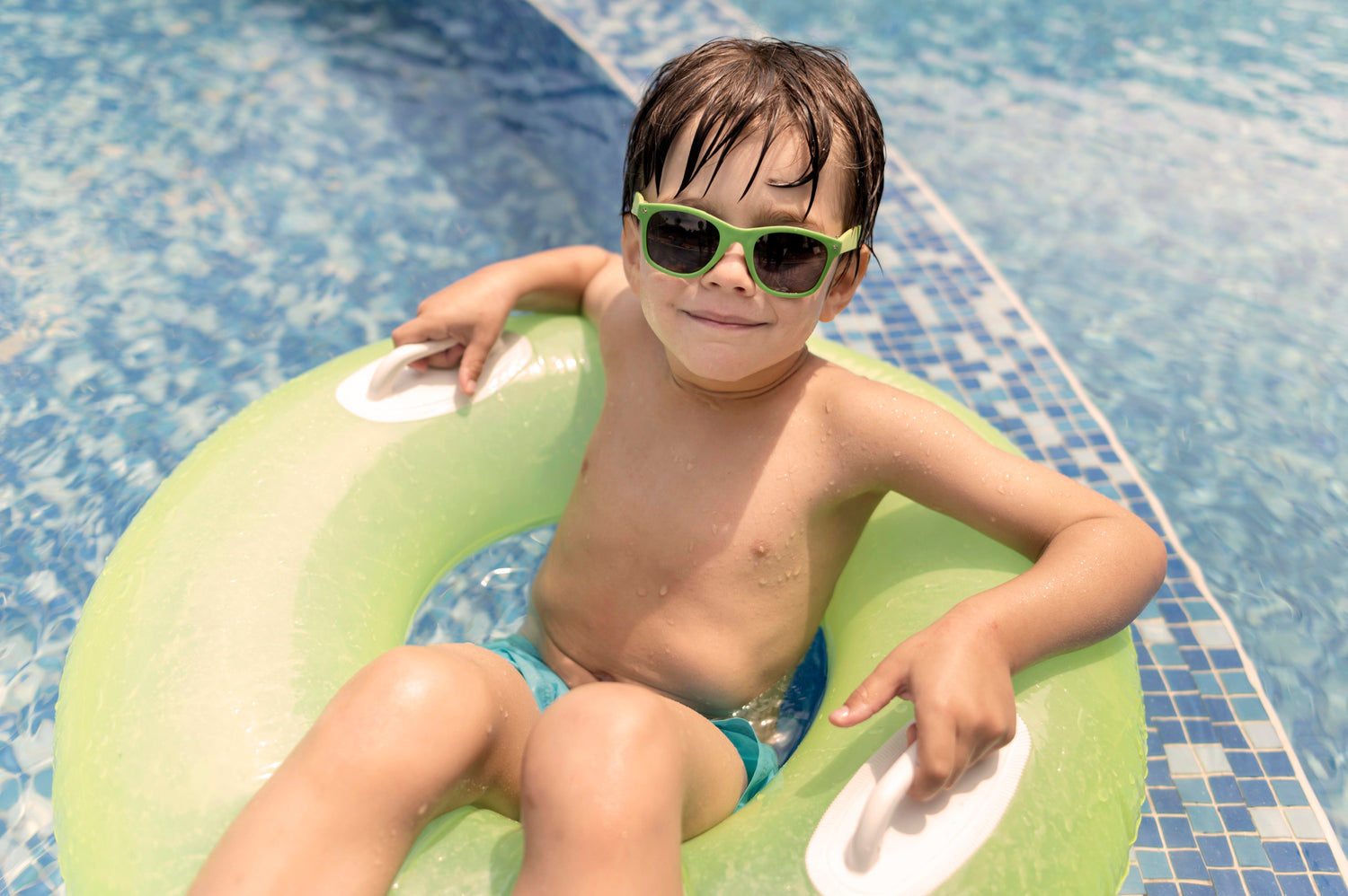 Enfant avec lunettes vertes assis sur une bouée dans une piscine
