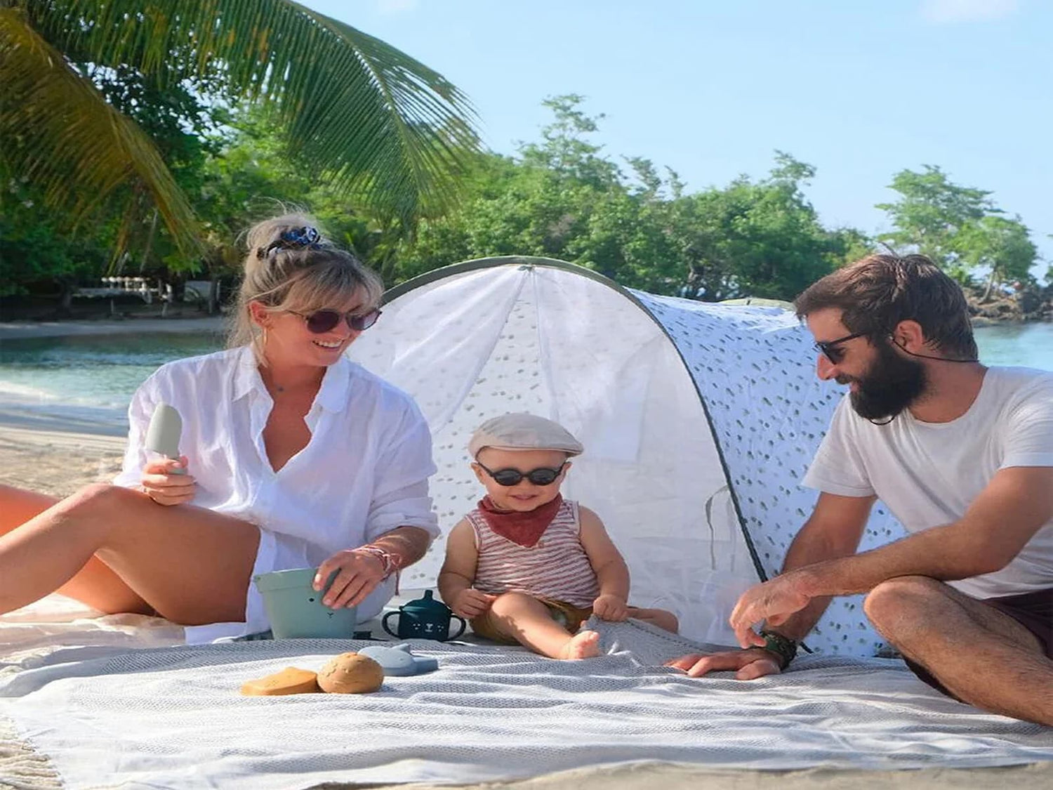 « Famille avec bébé sous une tente anti-UV sur la plage, accessoires soleil pour bébé »
