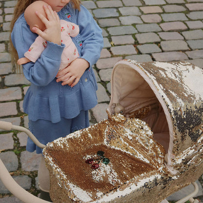Petite fille tenant son poupon à côté d’une poussette dorée pour poupée, jouet élégant et scintillant.