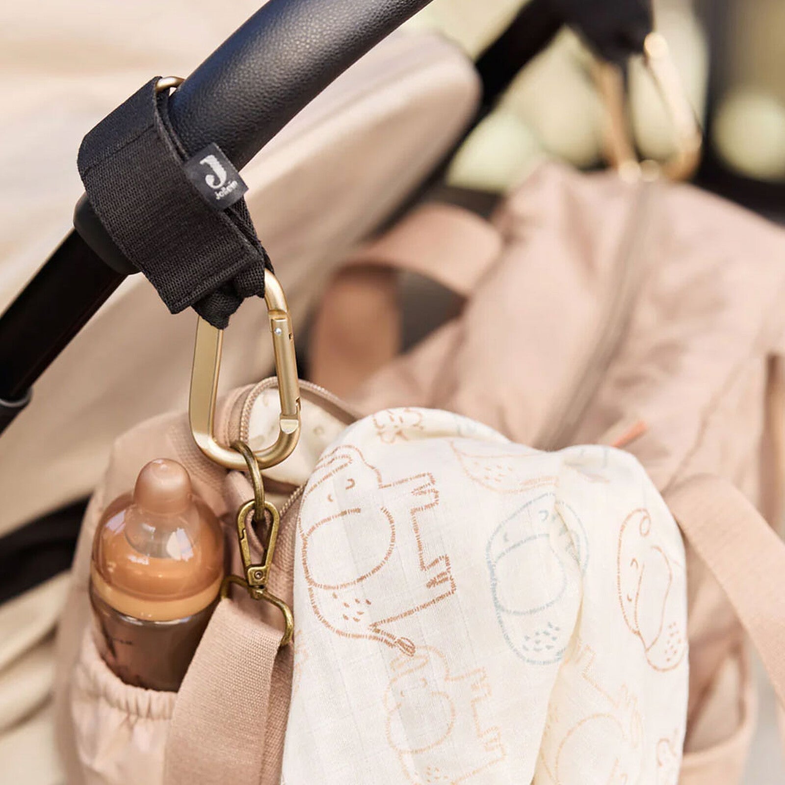 Sac à langer Jollein Embossed Lily Sand accroché à une poussette avec biberon