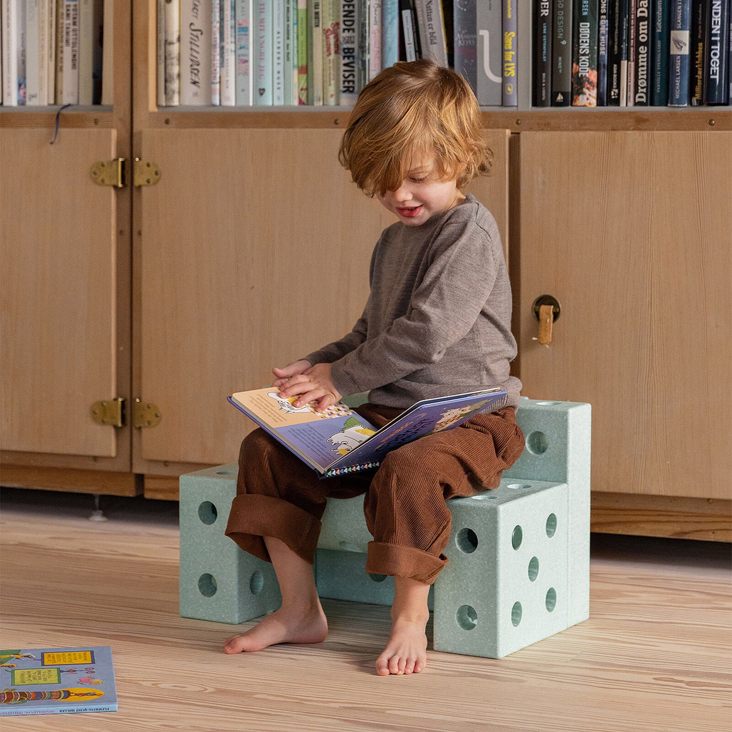 Enfant assis sur le tabouret modulable Mobu vert, idéal pour lire et jouer dans la chambre.