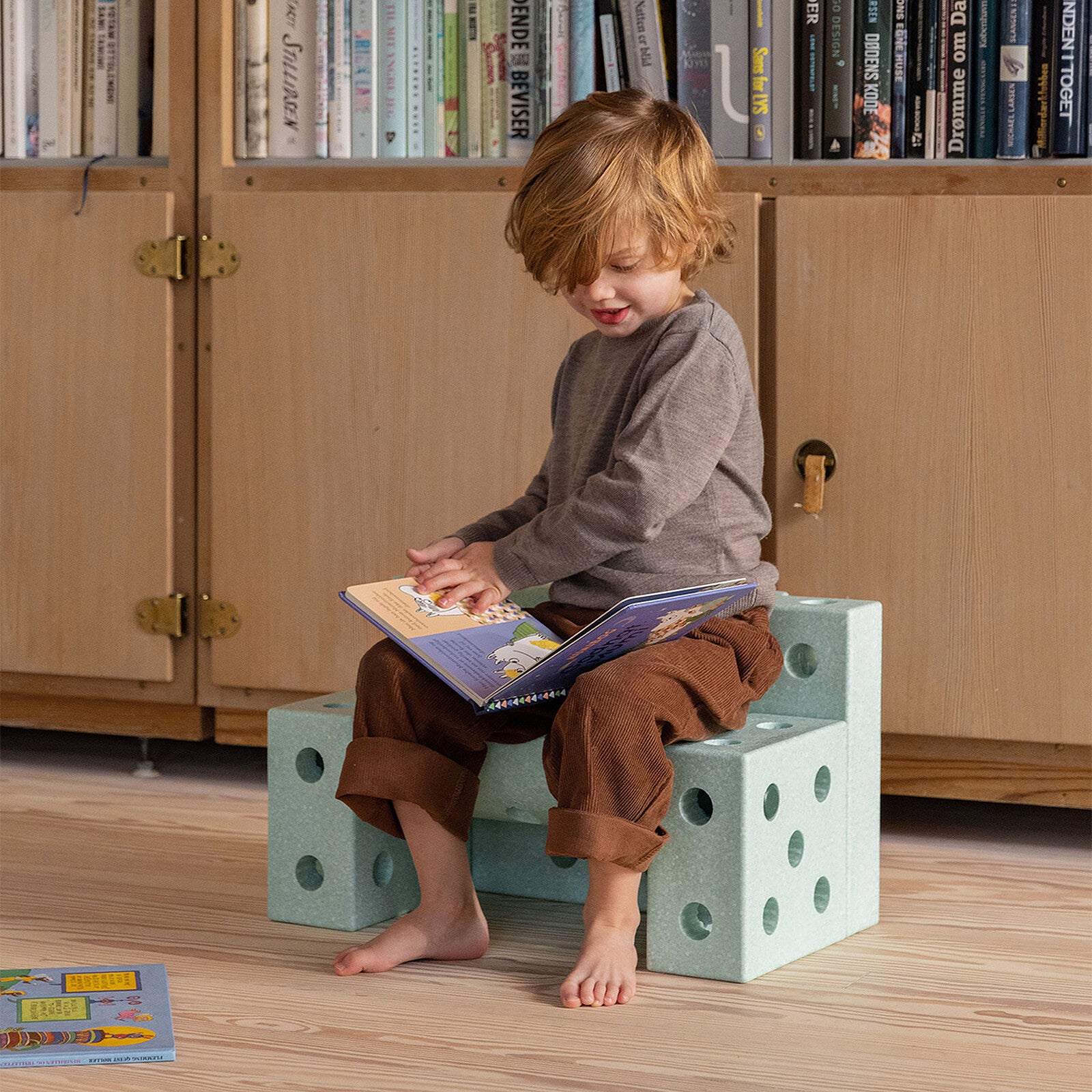 Enfant assis sur le tabouret modulable Mobu vert, idéal pour lire et jouer dans la chambre.