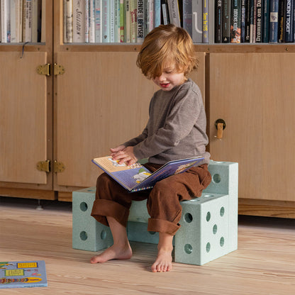 Enfant assis sur le tabouret modulable Mobu vert, idéal pour lire et jouer dans la chambre.
